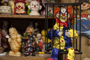 photo shows an evil clown in a cage with hundreds of other clown dolls behind it
